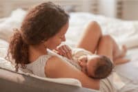 women breastfeeding her child on a bed