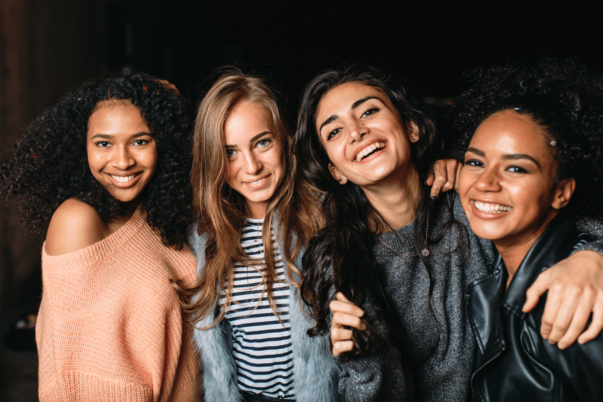 four young women of different races hugging and laughing