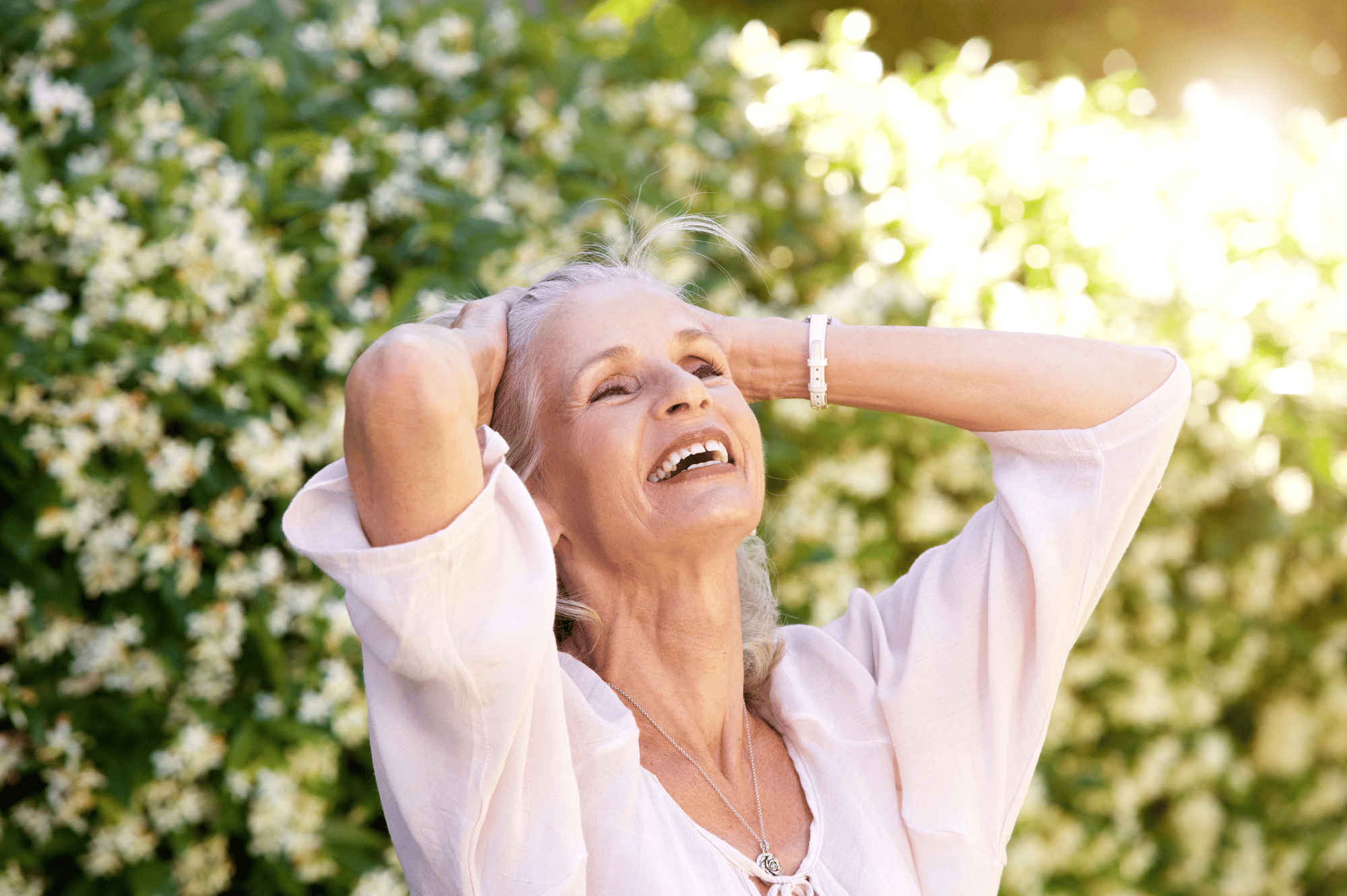 menopause-age woman stretching her arms above her head while standing in front of a flowering bush