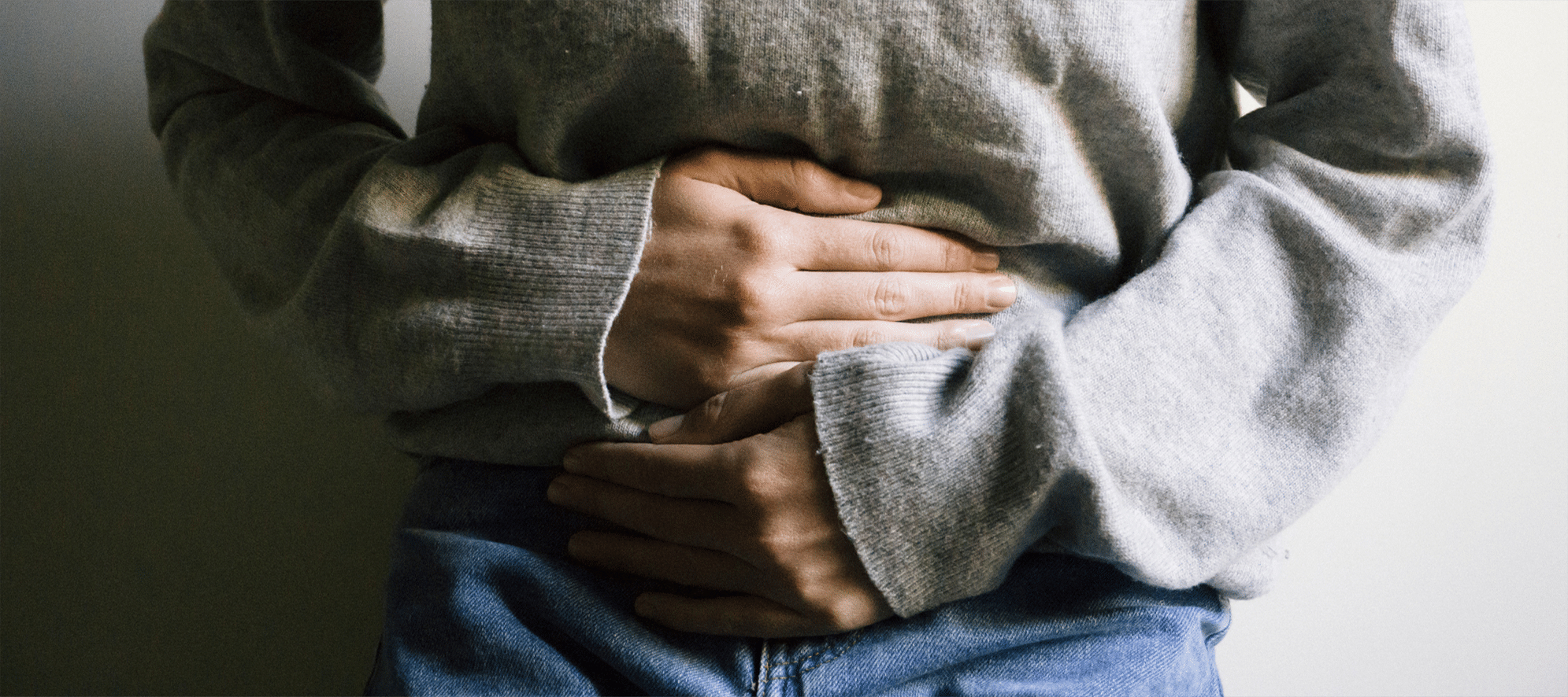 woman wearing a grey top and jeans, holding her pelvic area in pain