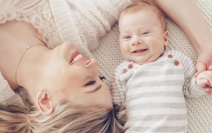 mother lying on a blanket with her baby. baby is looking at camera and mother is looking at baby.