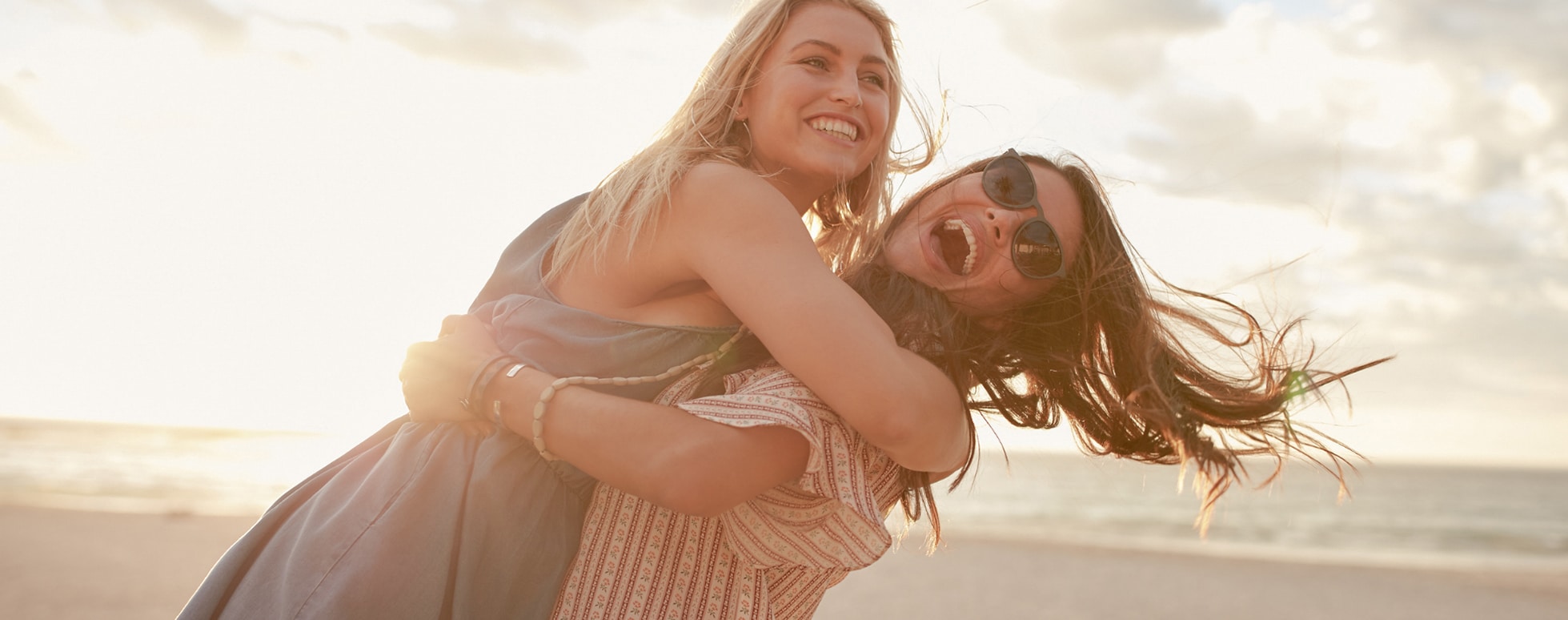 two women holding each other and laughing at the beach
