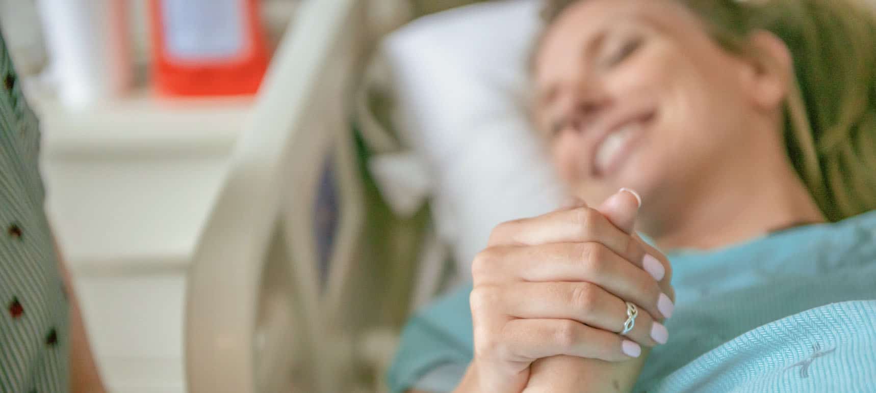 a pregnant woman lying in a hospital bed, holding hands with her support person.